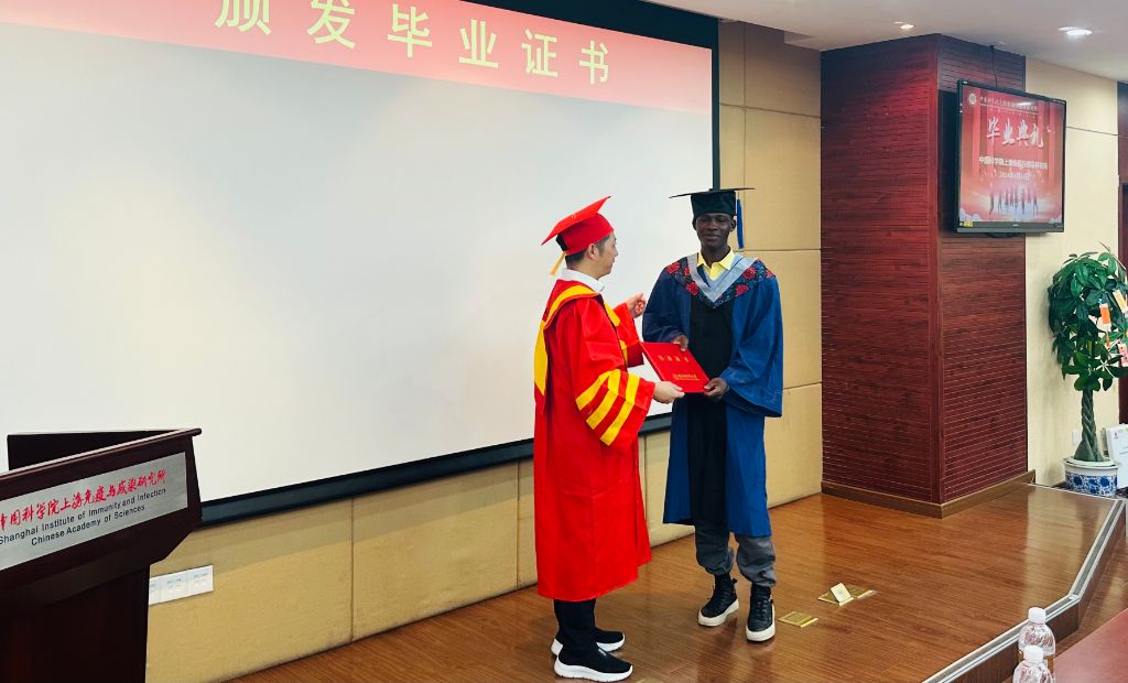 Receiving the MSc diploma on stage from a professor in red robes