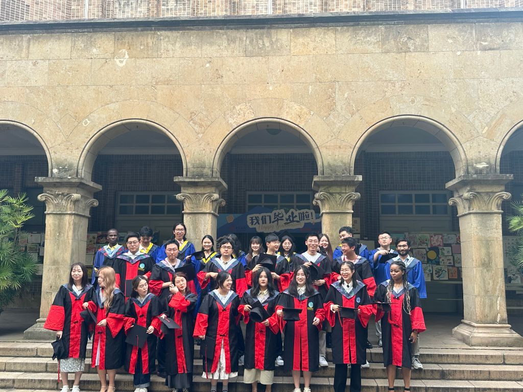 Cohort of graduates in blue and red robes standing under stone arches