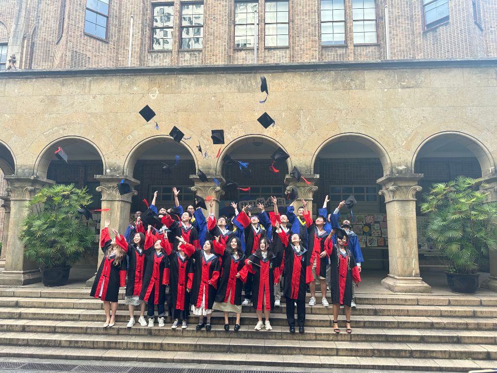 Graduating cohort throwing caps in the air on stone steps under arched columns